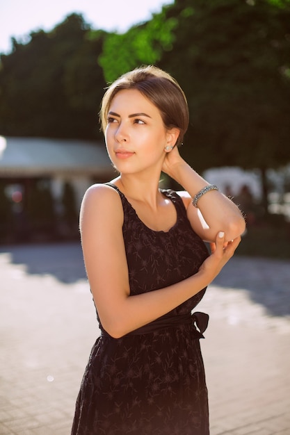 Femme brune élégante avec bronzage bronze posant dans la rue dans une robe à la mode