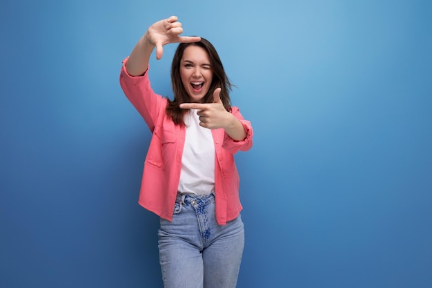 Femme brune élégante dans une chemise à la mode prend un selfie à l'aide d'un téléphone sur un fond de studio