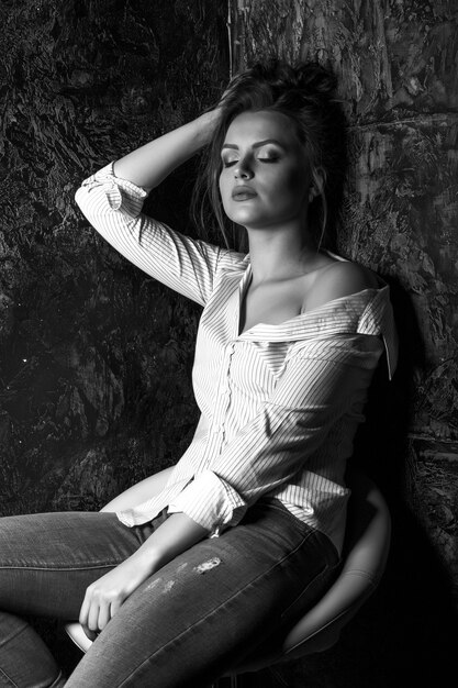 Une femme brune élégante avec du maquillage naturel porte une chemise qui pose au studio. Portrait noir et blanc