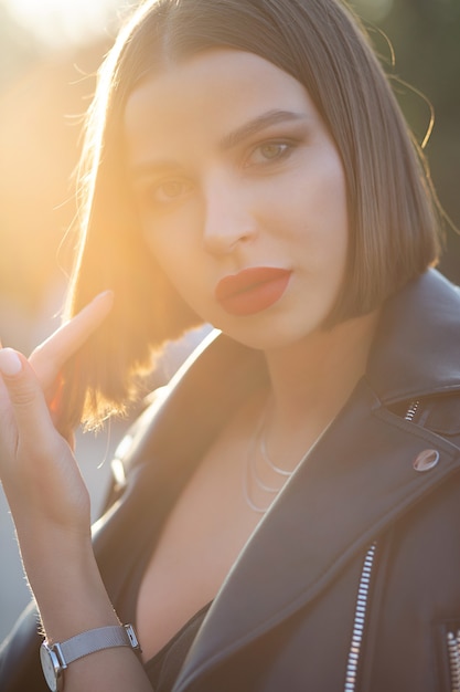 Femme brune élégante avec un maquillage lumineux posant dans une rue avec des reflets du soleil. Photo en gros plan