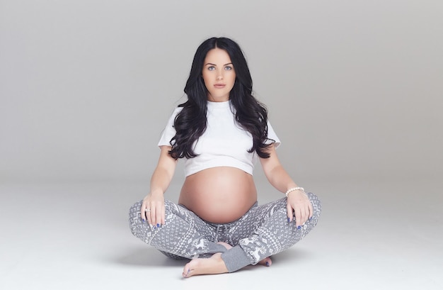 Femme brune enceinte assise avec les jambes croisées.