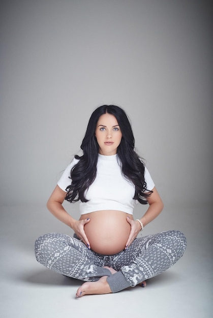 Femme brune enceinte assise avec les jambes croisées.