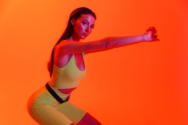 femme brune énergique portant des vêtements de sport ajustés faisant des exercices de gymnastique isolés sur un mur de néon orange