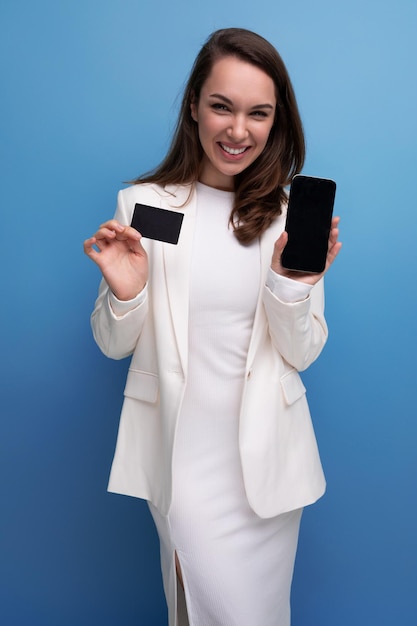 Une femme brune énergique en tenue de bureau paie l'achat à l'aide d'une carte et d'un téléphone