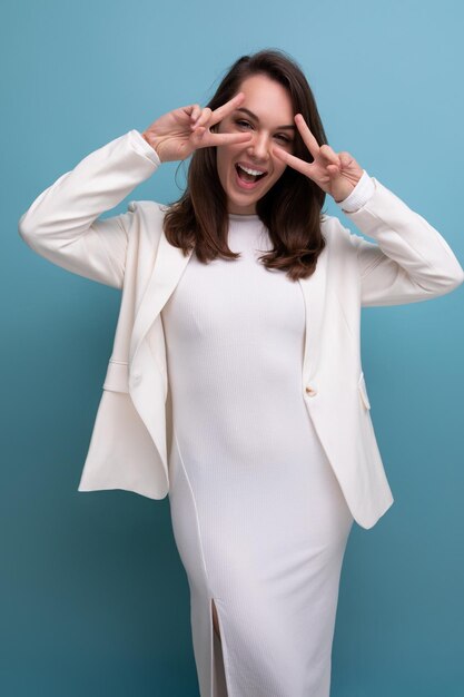 Femme brune européenne en robe blanche fait une grimace sur fond de studio