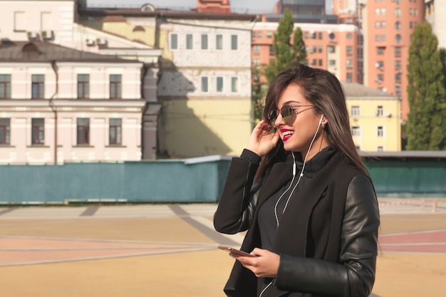 Une femme brune heureuse écoute de la musique sur un téléphone portable, marchant dans la rue