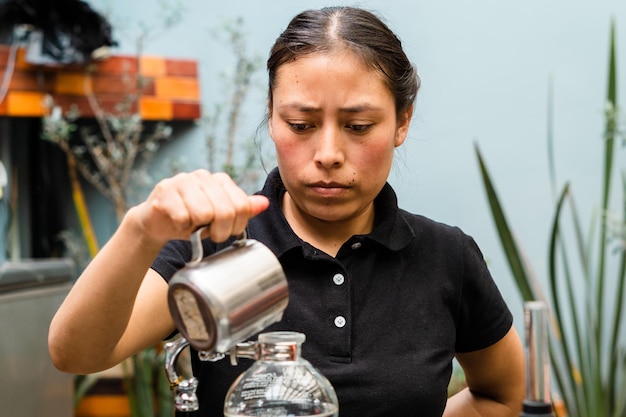 Femme brune hispanique avec une expression sérieuse préparant du café dans une cafétéria.