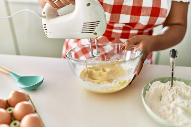 Femme brune hispanique préparant un gâteau avec un fouet électrique à la cuisine