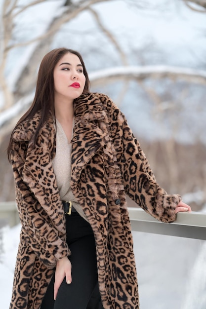 Femme brune en manteau de fausse fourrure avec motif léopard et jeans noirs courbant debout regardant loin