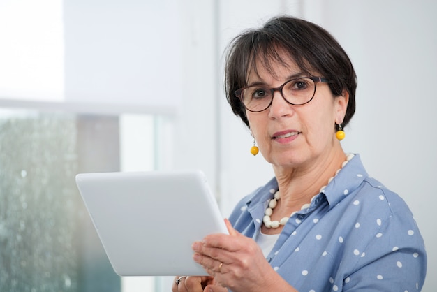 Femme brune mature assise sur un canapé à l'aide d'une tablette numérique