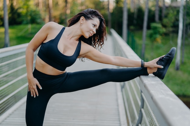 Une femme brune mince et sportive vêtue d'un haut court et de leggings étire les jambes sur le pont se réchauffe avant la pose de course du matin en plein air veut avoir un corps mince et une bonne santé. Faire des exercices