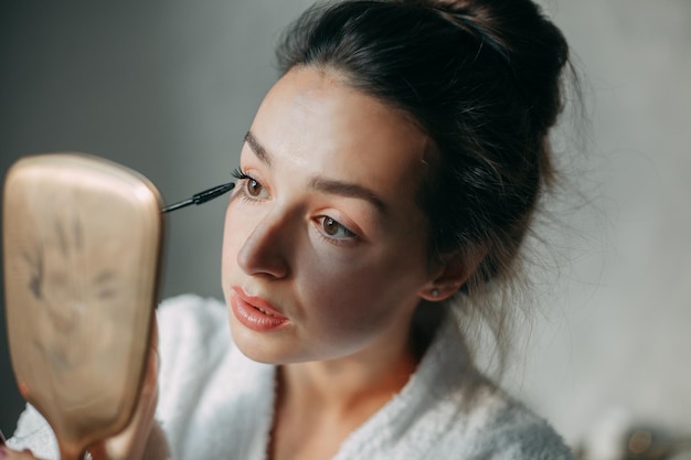 Une femme brune peint des cils avec du mascara noir