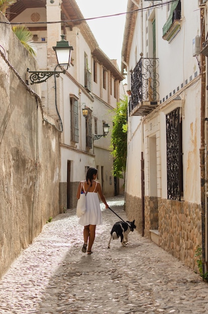 Une femme brune en robe blanche apprécie une promenade paisible dans les rues d'une ville européenne avec son chien