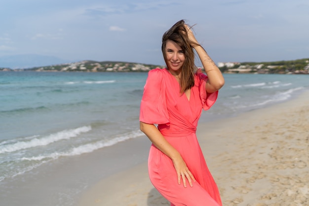 Femme brune séduisante avec tatoo sur place en robe rose posant sur la plage.