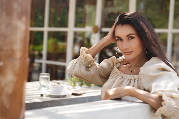 Femme brune sensuelle avec un sourire rêveur, se retourne à la recherche de la caméra dans un café.