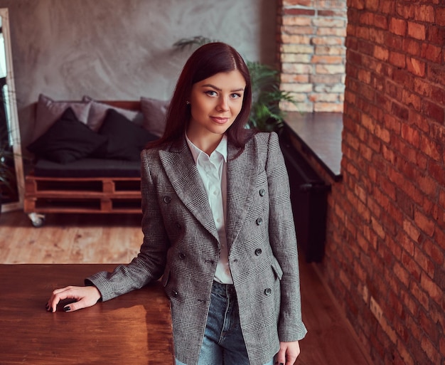 Femme brune sensuelle vêtue de vêtements à la mode posant dans une pièce avec intérieur loft, regardant la caméra.