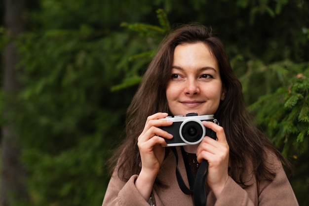 Femme brune souriant mystérieusement avec appareil photo numérique