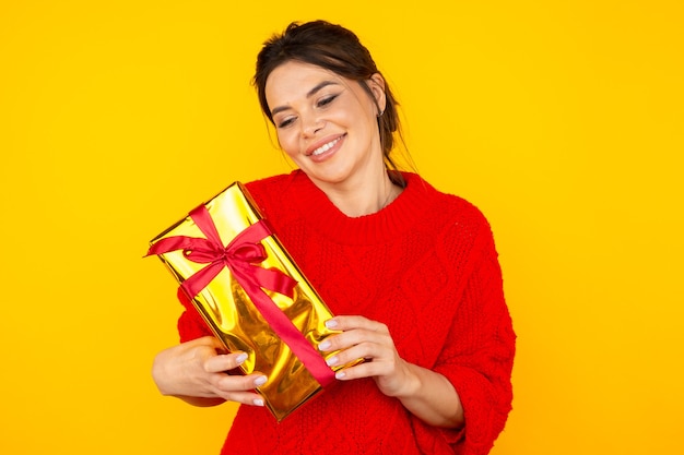 Femme brune souriante avec gros cadeau dans le studio jaune.