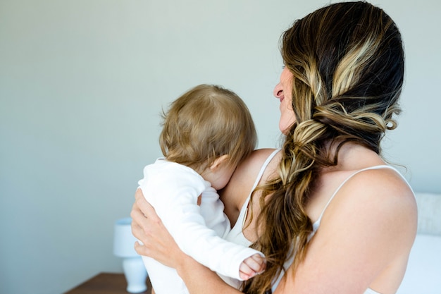 femme brune souriante tenant un bébé contre son épaule