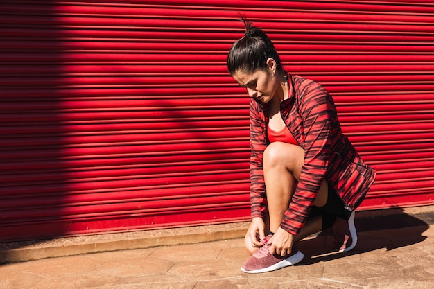 Une femme brune en tenue de sport rouge attache ses lacets avant de courir