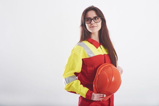 Femme brune en uniforme orange et jaune se dresse contre le mur blanc dans le studio