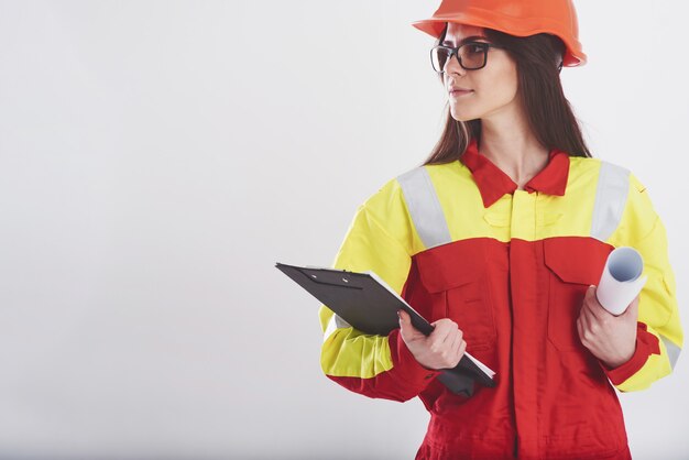 Femme brune en uniforme orange et jaune se dresse contre le mur blanc dans le studio