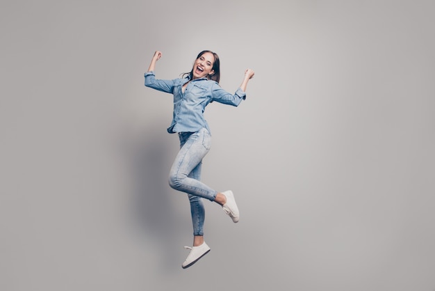 Femme brune avec veste en jean posant contre le mur gris