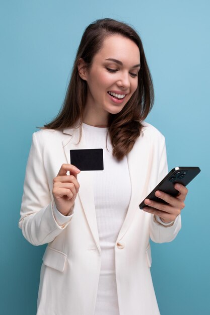 Une femme brune vêtue d'une robe utilise un transfert d'argent électronique à l'aide d'une carte et d'un smartphone