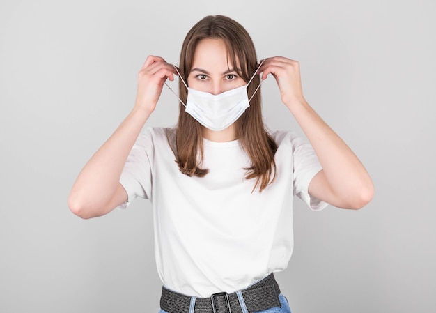 Une femme brune vêtue d'un t-shirt blanc et d'un jean porte un masque anti-virus pour que les autres n'infectent pas les autres avec le coronavirus