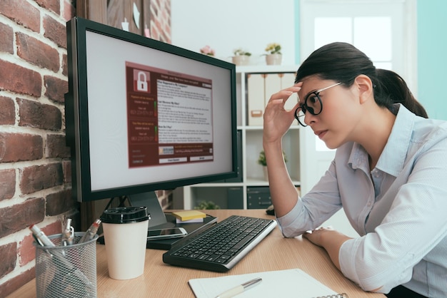 femme de bureau assez attrayante pensant à une solution de travail lorsque son ordinateur de travail de l'entreprise se fait envahir par le virus du chantage.