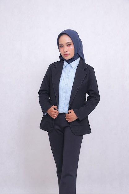 Une femme de bureau mature asiatique portant un hijab et une chemise bleue se tient debout en souriant élégamment tenant une veste inférieure