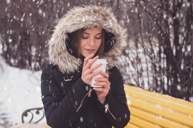 Femme buvant du café chaud ou du thé dans une tasse sous des flocons de neige en hiver