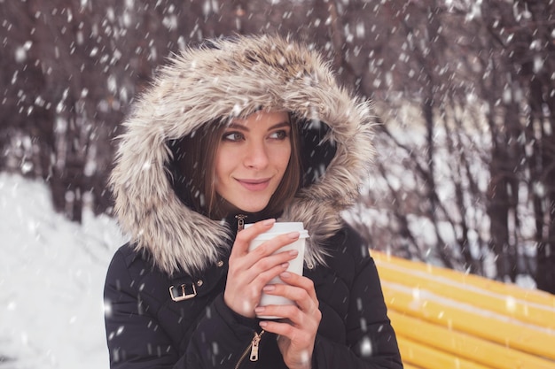 Femme buvant du café chaud ou du thé dans une tasse sous des flocons de neige en hiver