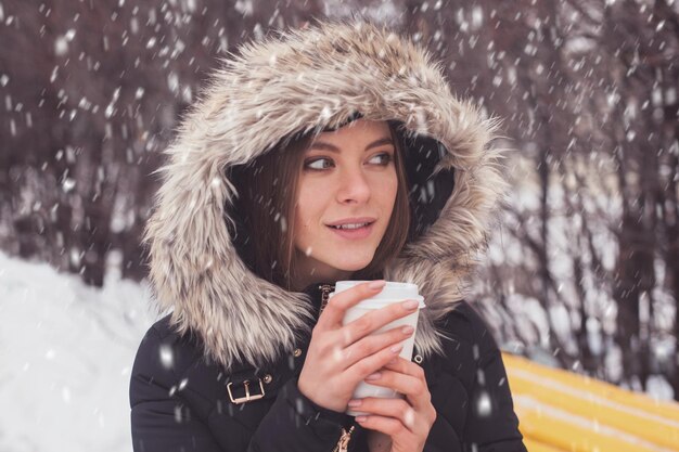 Femme buvant du café chaud ou du thé dans une tasse sous des flocons de neige en hiver