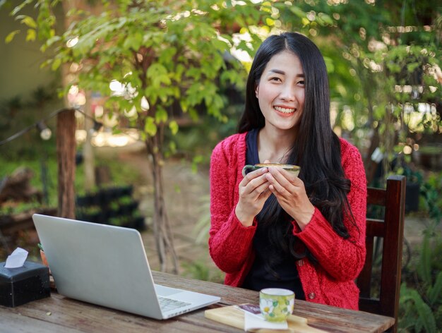 femme buvant du café et de travailler avec un ordinateur portable dans le jardin