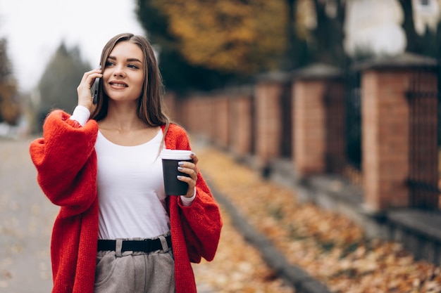 Femme buvant du café et utilisant le téléphone et marchant dans la rue d'automne