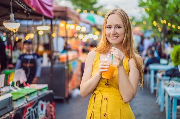 Femme buvant du jus d'orange sur le marché asiatique