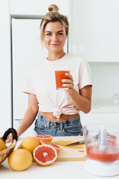 Femme buvant du jus de pamplemousse maison fraîchement pressé dans une cuisine blanche