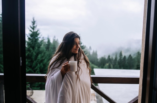 Photo femme buvant du thé sur un balcon confortable d'une maison de campagne