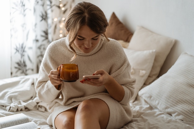 Femme buvant du thé chaud et utilisant le téléphone. Style de vie confortable.