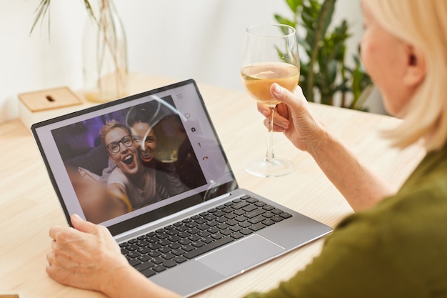 Femme buvant du vin et parlant à ses amis en ligne sur écran d'ordinateur, ils célèbrent un événement