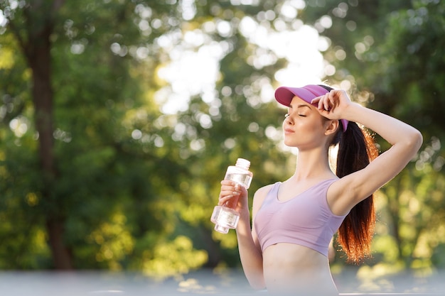 Femme buvant de l'eau à la bouteille après l'entraînement au parc pour rester hydratée