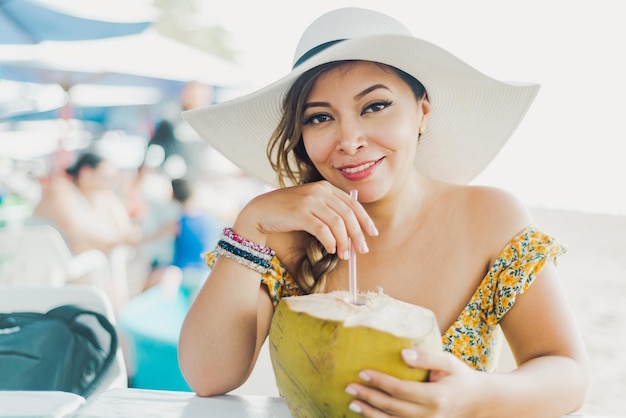 Femme buvant de l'eau de coco. Femme portant un chapeau de plage buvant de l'eau de coco avec une paille.