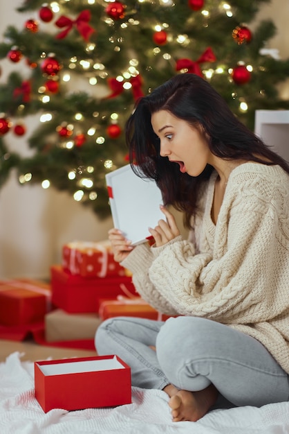 Femme avec cadeau dans la boîte-cadeau près de l'arbre de Noël à la maison
