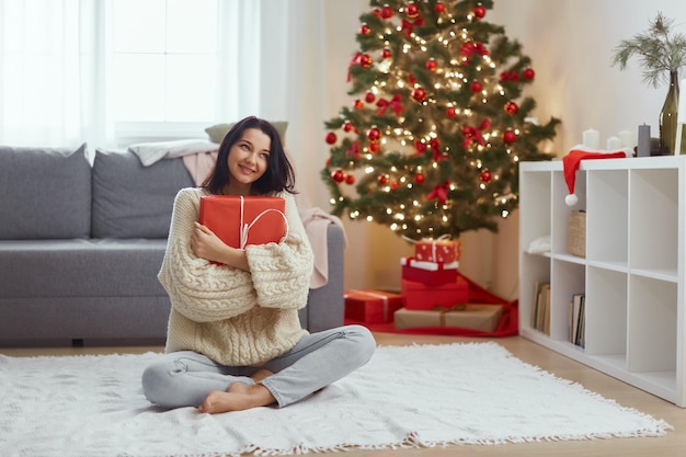 Femme avec cadeau dans la boîte-cadeau près de l'arbre de Noël à la maison