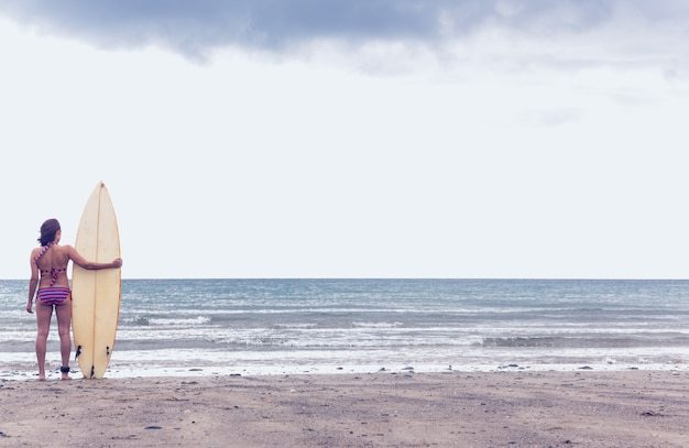 Femme calme en bikini avec planche de surf sur la plage