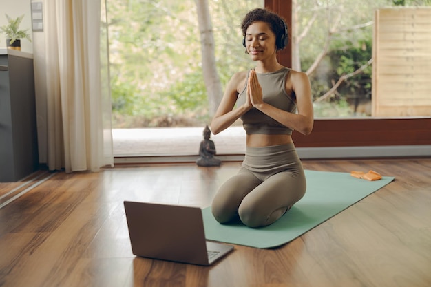 Une femme calme avec des écouteurs et des vêtements de sport méditant et pratiquant le yoga à la maison assise sur un tapis