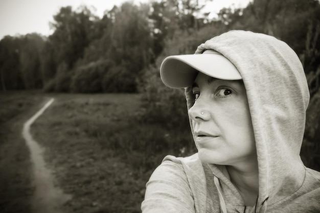 Femme en capuche et casquette dans le parc parmi les arbres en noir et blanc