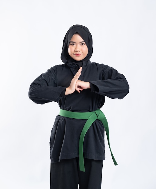 Une femme à capuche portant un uniforme de pencak silat avec une ceinture verte effectue des gestes respectueux de la main