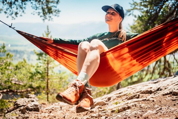 Femme avec capuchon reposant dans un hamac confortable dans les montagnes Se détendre sur un hamac orange entre deux pins en profitant de la vue sur la nature